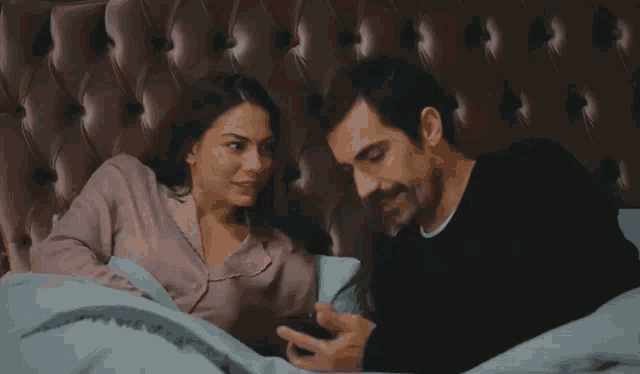 a man and a woman are laying in bed looking at a phone