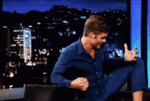 a man in a blue shirt is sitting on a couch with his legs crossed
