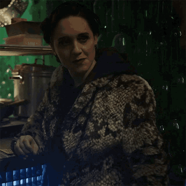 a woman wearing a fur coat is standing in front of a green wall