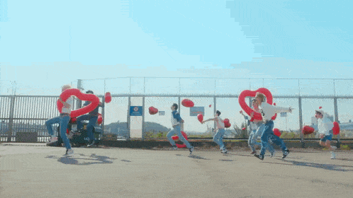 a group of people are holding red balloons in the shape of a heart .