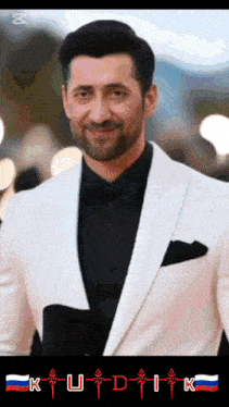 a man in a white suit and black shirt with the letters k u d i k below him