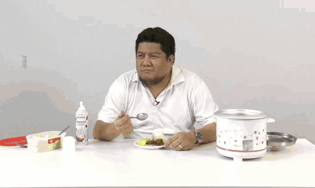 a man sitting at a table with a spoon in his hand and a bottle of popcorn sauce behind him