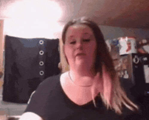 a woman in a black shirt is making a funny face in front of a black curtain .