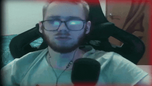 a man with glasses and a beard is sitting in a chair with a microphone