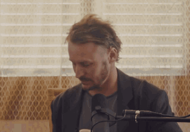 a man with a beard is sitting in front of a microphone in a room