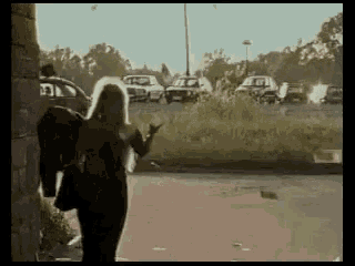 a woman with blonde hair is walking down a street in front of a parking lot