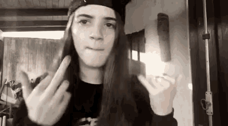 a girl with long hair is wearing a hat and making a funny face while giving the middle finger .