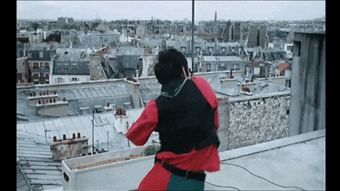 a man in a red and black jacket is standing on a roof overlooking a city