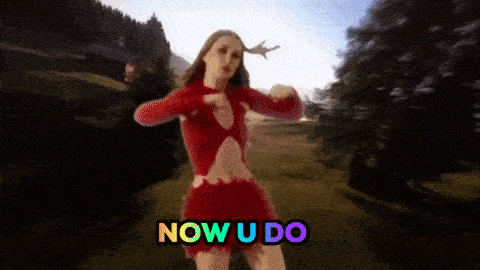 a woman in a red dress is dancing in a field with the words now u do behind her