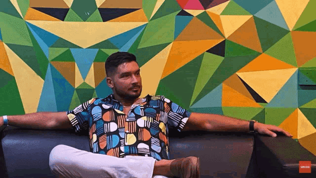 a man sits on a couch in front of a wall with geometric shapes