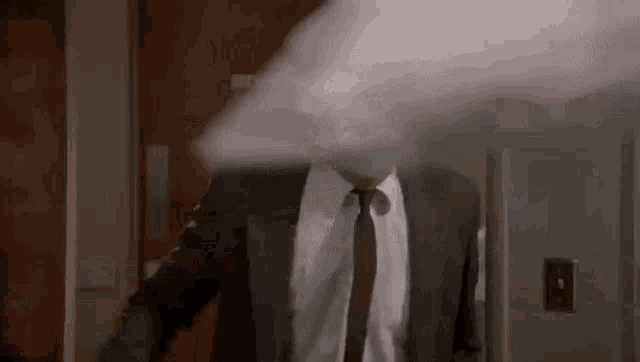 a man in a suit and tie is standing in a room with smoke coming out of his mouth .