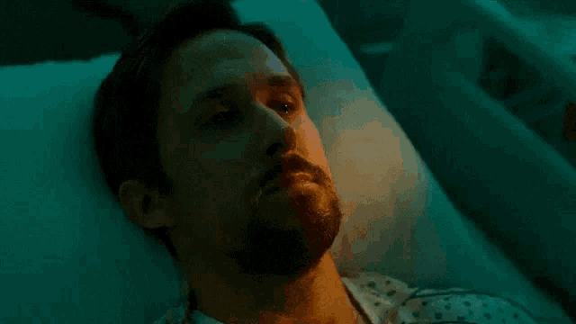 a man with a beard is laying in a hospital bed and looking at the camera .