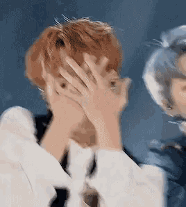 a man is covering his face with his hand while another man looks on .