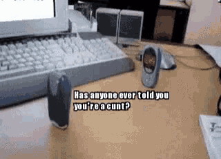 a keyboard is on a desk next to a cell phone that says " has anyone ever told you you 're a cunt "