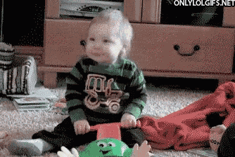 a baby wearing a green and black striped shirt with a truck on it is sitting on the floor