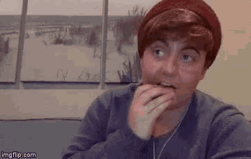 a man wearing a red hat and a blue sweater is eating a piece of food .