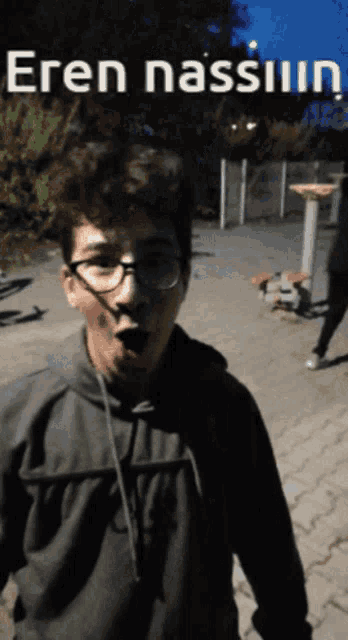 a man with glasses and a surprised look on his face stands in front of a sign that says " eren nassiun "