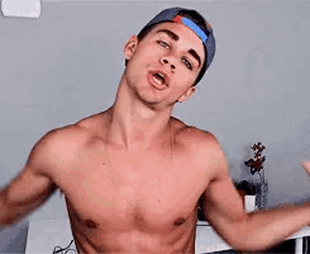 a shirtless man is flexing his muscles while wearing a hat .