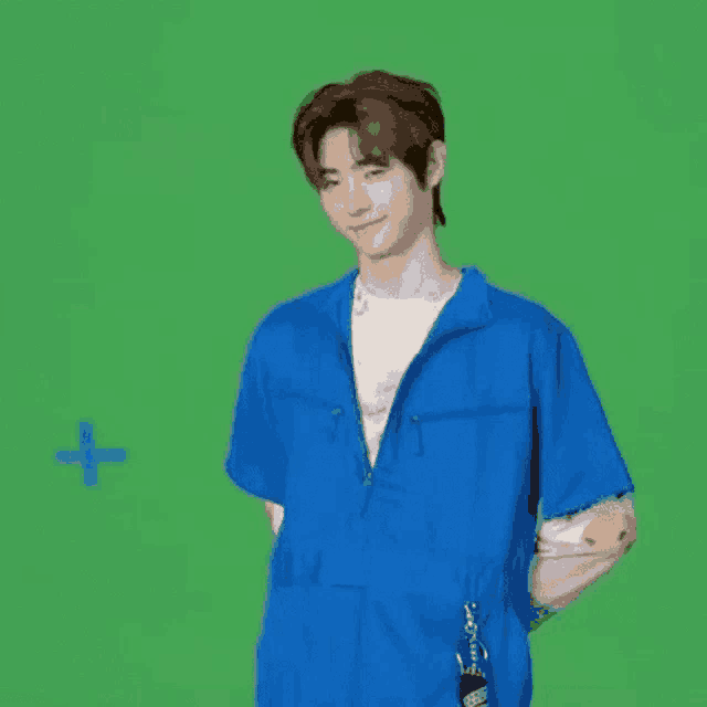 a young man wearing a blue jumpsuit is standing in front of a green screen .