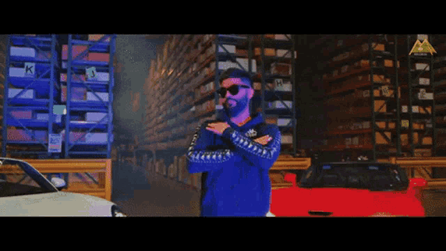 a man wearing sunglasses and a blue sweater is standing in front of a red car