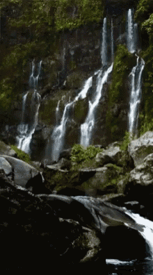 a waterfall is surrounded by rocks and trees in the woods