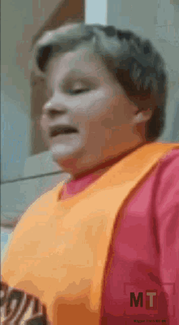 a young boy wearing an orange bib and a pink shirt is making a face .