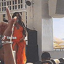 a woman in an orange dress is giving a peace sign while a man takes a picture of her ..
