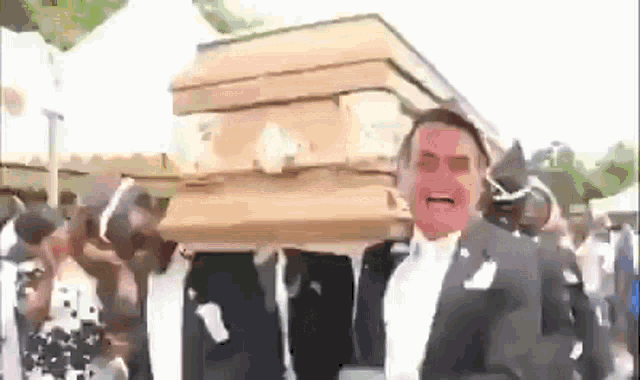 a man in a tuxedo is carrying a coffin with a coffin on his head .