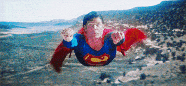a man dressed as superman is flying through the air over a desert landscape .