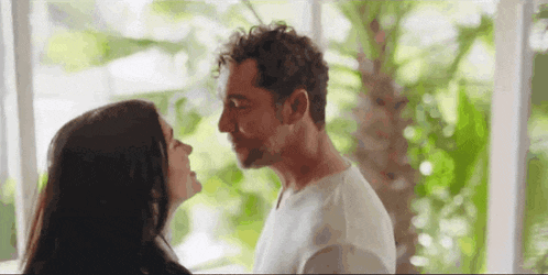 a man and a woman are kissing each other in front of a window .