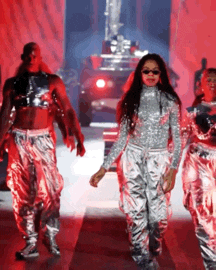 a group of dancers are walking down a runway with a car in the background