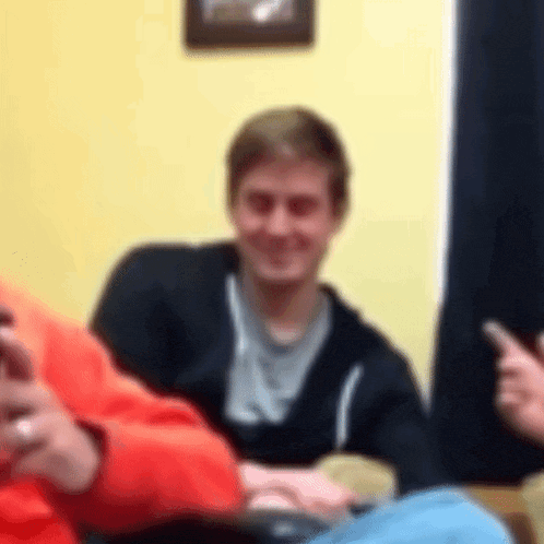 a blurry picture of a man sitting on a couch with a cell phone in his hand .