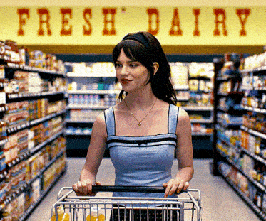a woman pushing a shopping cart in a grocery store under a sign that says fresh dairy