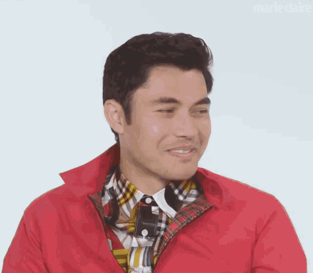 a close up of a man wearing a red jacket and a plaid shirt .