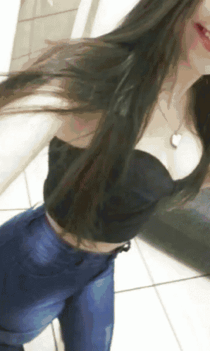 a woman in a black crop top and blue jeans takes a selfie