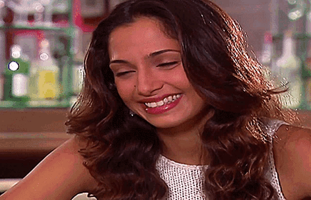 a woman with long brown hair is smiling and wearing a white top