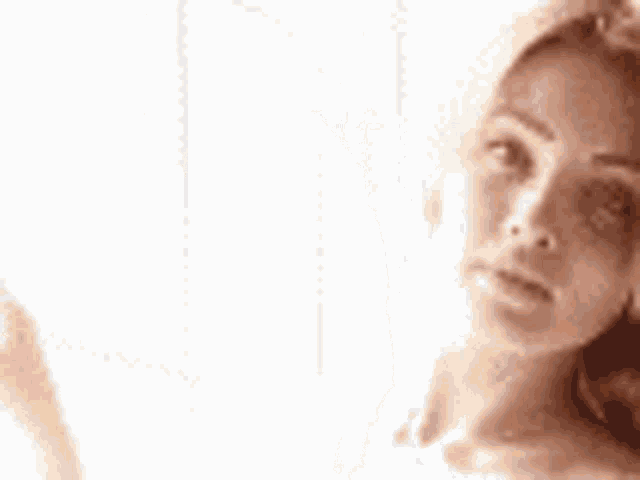 a woman is standing in front of a window with her hands up and looking at the camera .