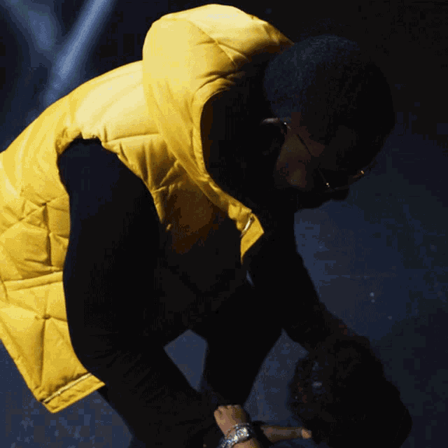 a man wearing a yellow vest is kneeling down and looking down