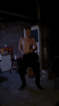 a shirtless man is dancing in a dark room holding a bottle of beer .