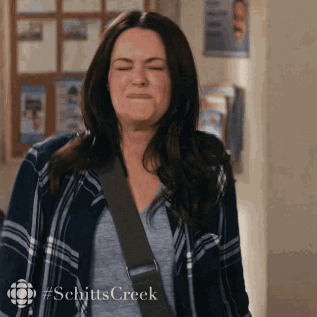 a woman wearing a plaid shirt is making a funny face with #schitts creek written in the corner