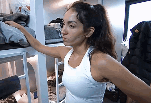 a woman in a white tank top is standing in a room