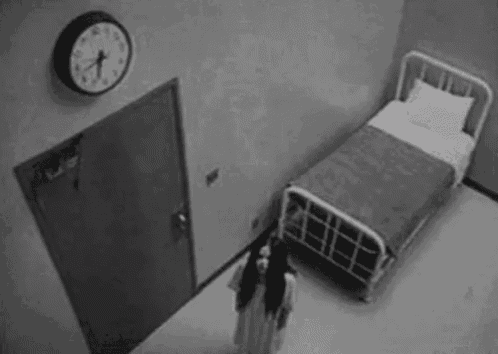 a black and white photo of a woman standing in a hospital room next to a bed .