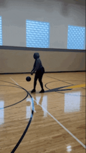 a person is dribbling a basketball on a court with a window in the background