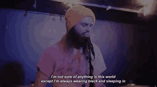 a man with a beard is singing into a microphone while wearing a yellow beanie .