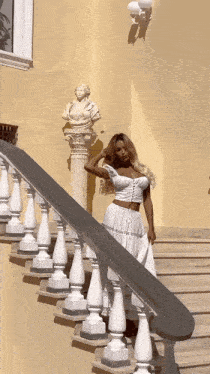 a woman in a white dress stands on a set of stairs with a statue in the background