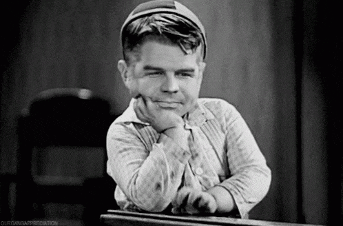 a black and white photo of a very small man leaning on a desk with his hand on his chin .