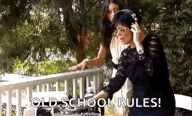 a woman wearing headphones is talking on a cell phone while standing next to another woman on a porch .