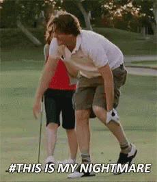 a man is kneeling down on a golf course with a woman standing behind him .