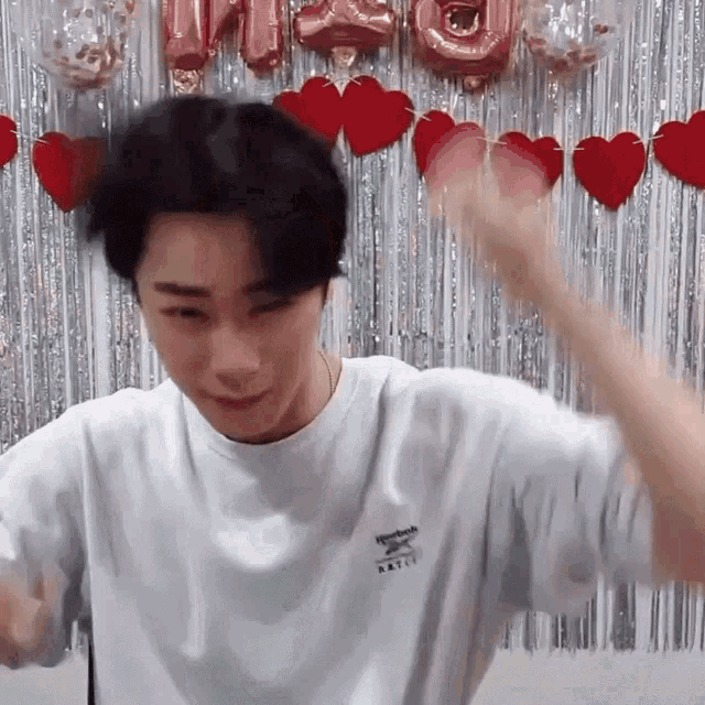 a man wearing a white reebok shirt is standing in front of a heart shaped curtain