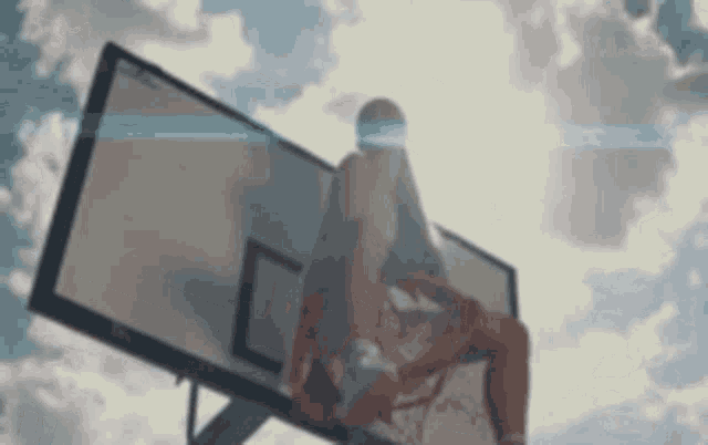 a man is sitting on top of a basketball hoop with a basketball in his hand .